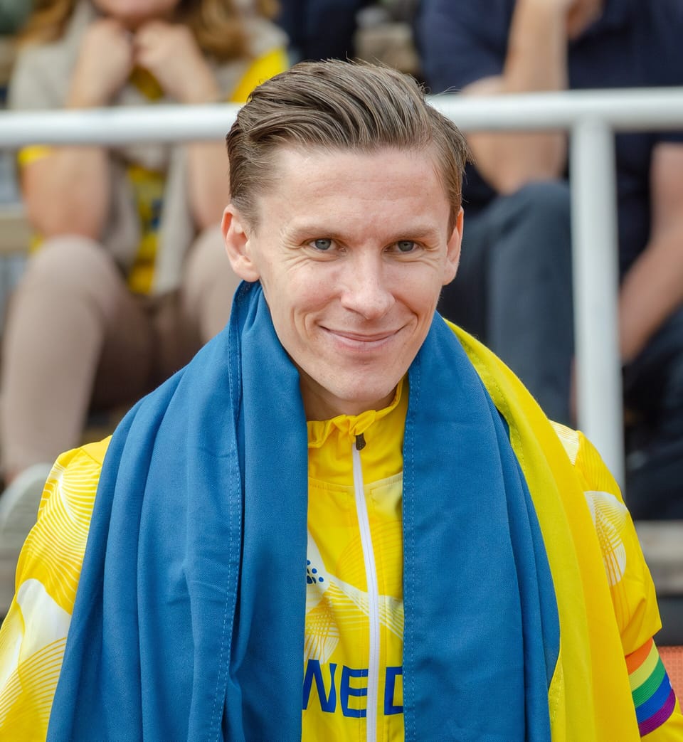 Andreas Almgren smiling with a Swedish flag around his shoulders