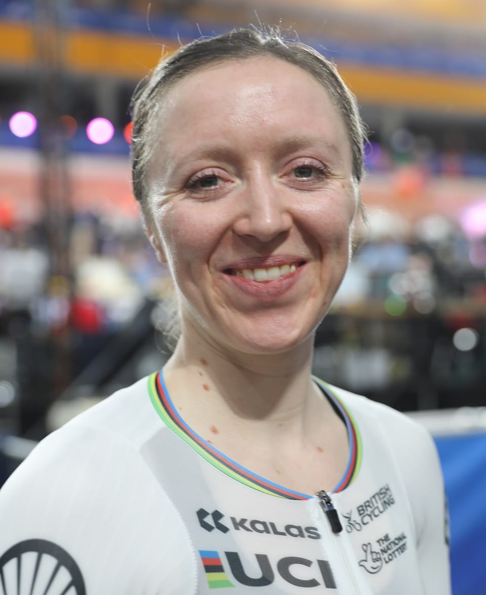 Anna Morris smiling in a white Great Britain skinsuit with rainbow bands on the collar, in a velodrome