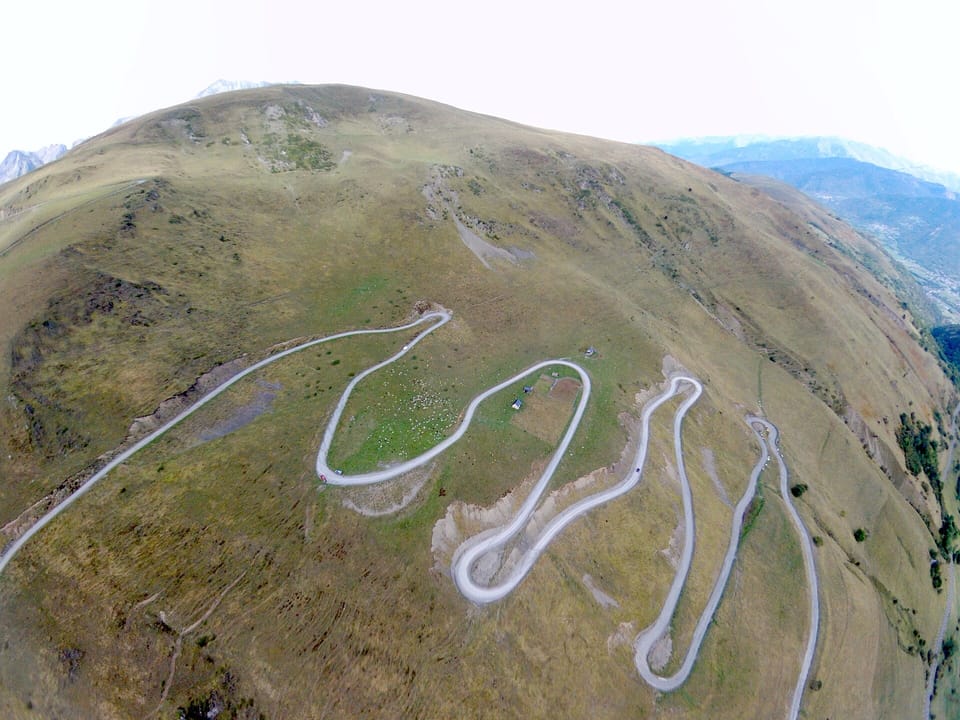 Aerial view of a narrow road zigzagging in tight hairpins up a grassy mountainside in the Pyrenees