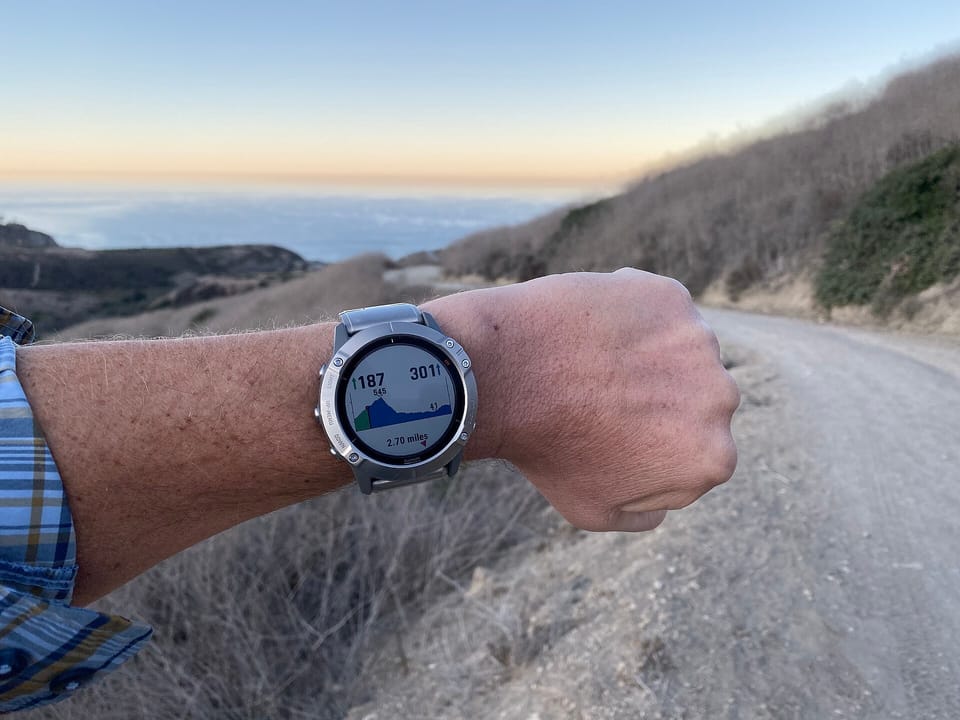 A Garmin outdoor watch with a solar lens worn on a wrist, with hills and sea behind