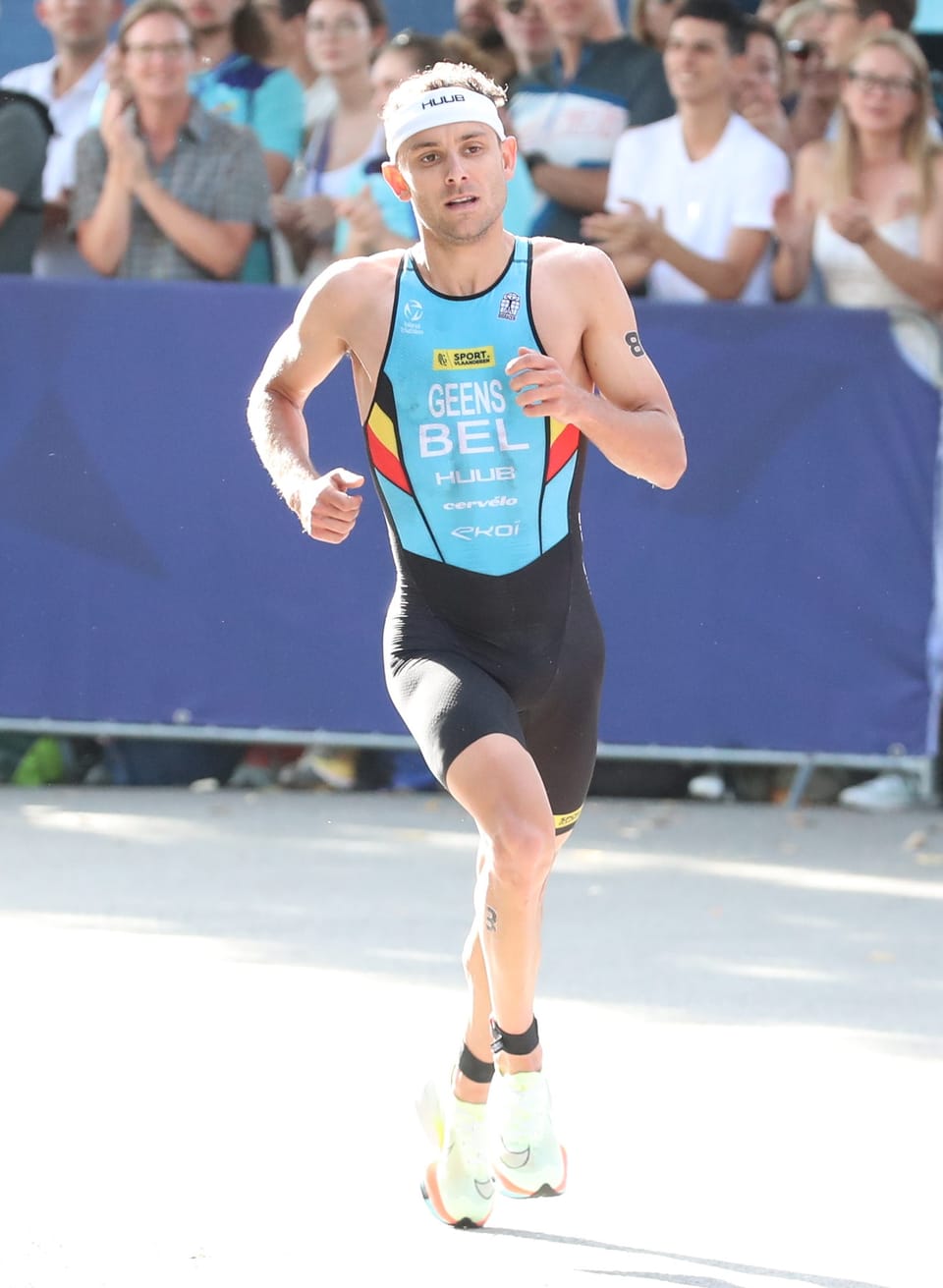 Jelle Geens running in a Belgian tri-suit past spectators behind a barrier