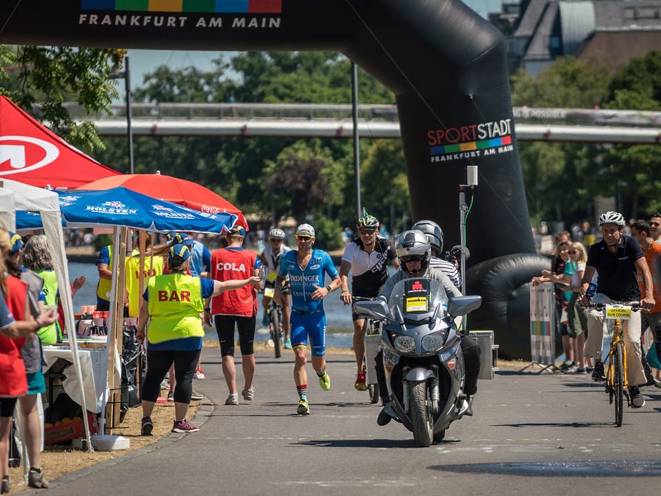 Patrick Lange running past spectators beside a race motorbike at Ironman Frankfurt