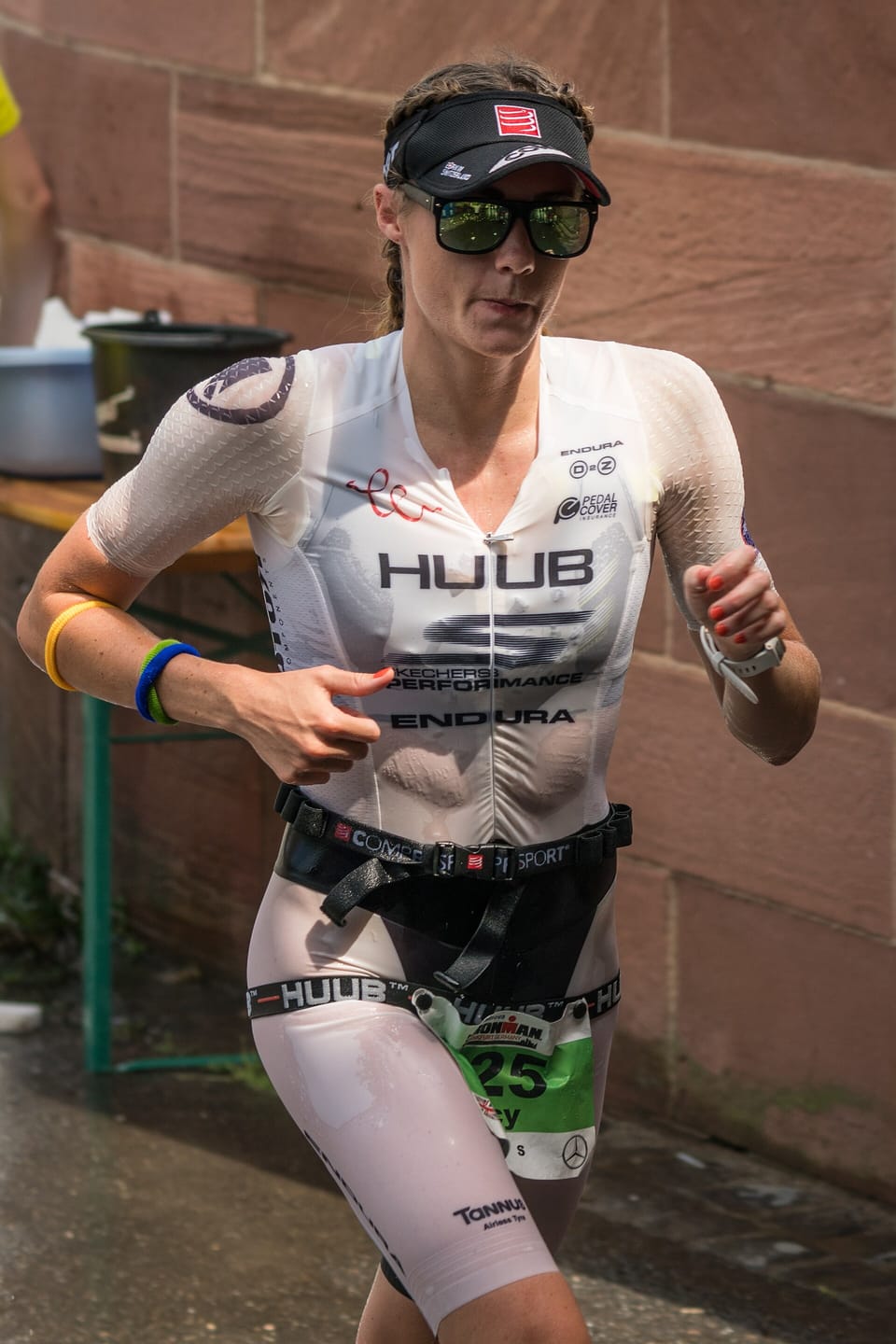 Lucy Charles-Barclay running in a white race suit, cap and sunglasses past a sandstone wall