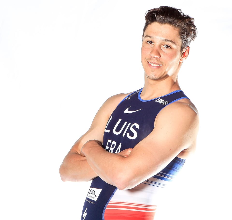 Vincent Luis with arms folded, wearing a French team race suit, in a white photo studio