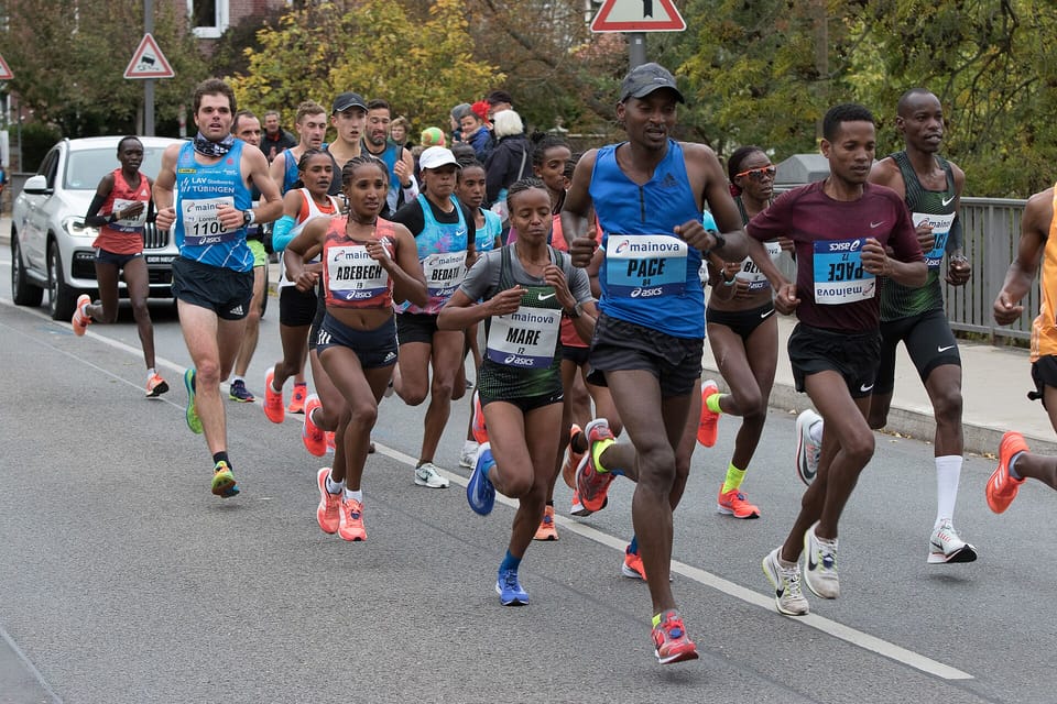 A group of elite women marathon runners with male pacemakers on a tree-lined Frankfurt street
