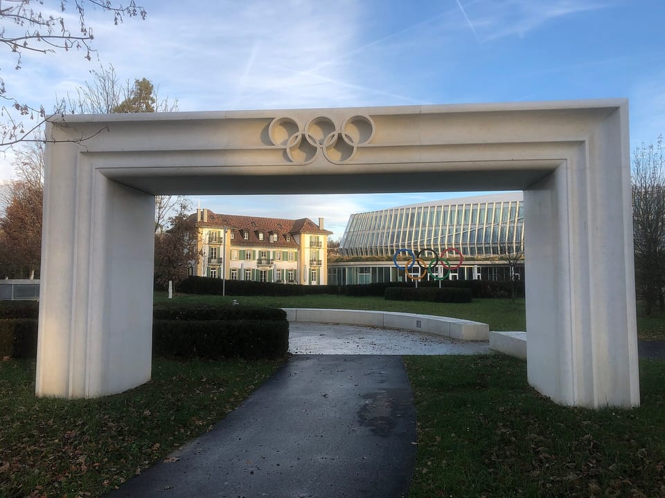 A white stone arch bearing the Olympic rings in front of Olympic House, the IOC headquarters in Lausanne
