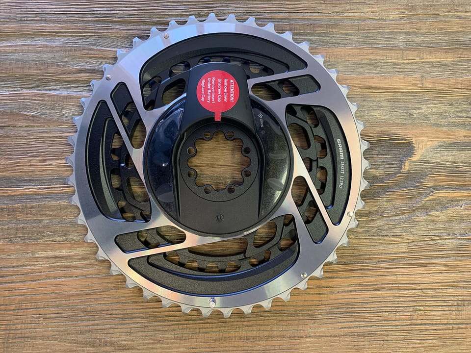 A SRAM Red AXS chainring and power meter lying on a wooden surface