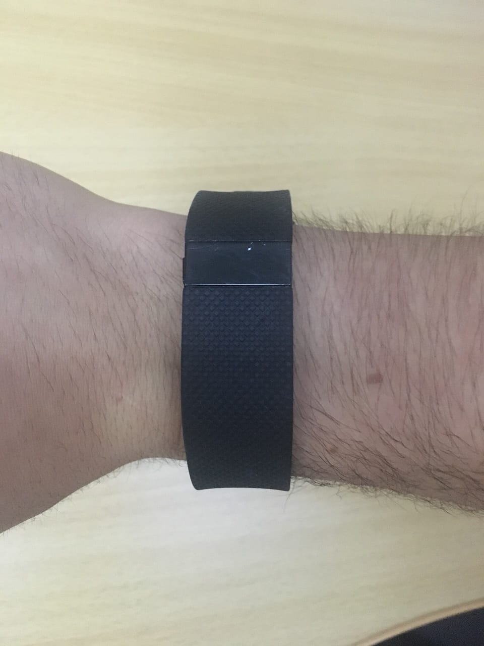 A black fitness band with its display switched off, worn on a forearm