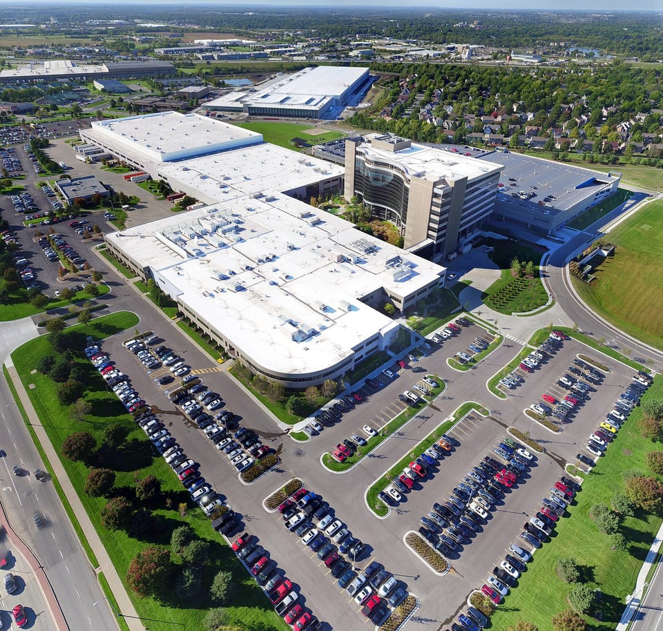 Aerial view of a large office and warehouse campus surrounded by car parks and trees