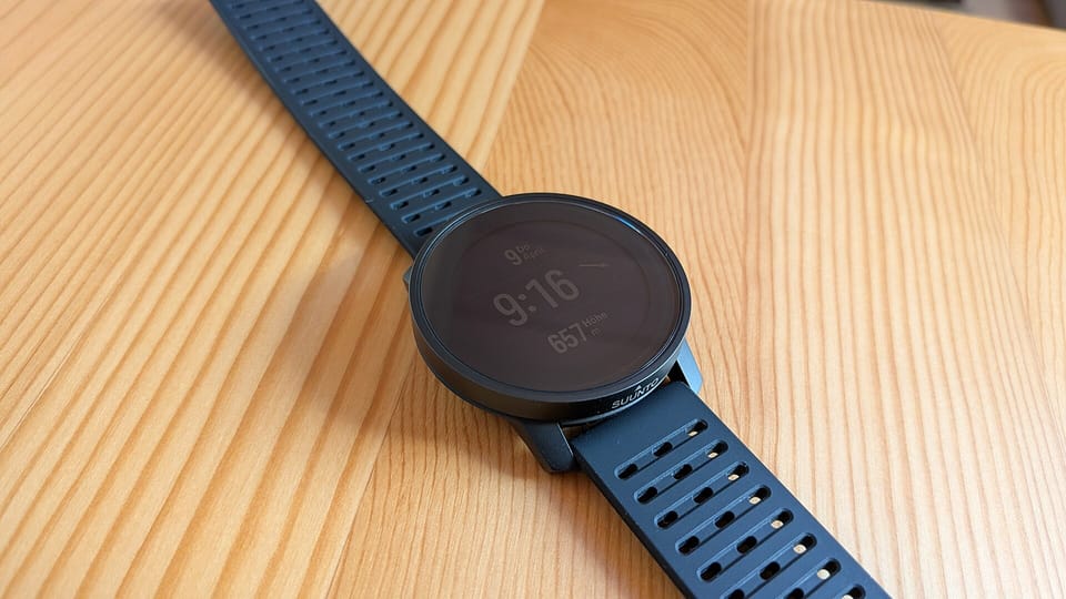 A black round sports watch with a dark silicone strap lying on a wooden table