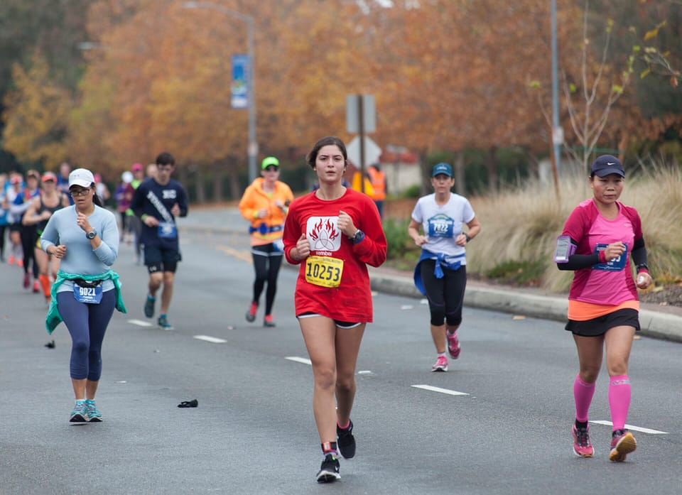 Runners with race bibs on a tree-lined suburban road in autumn