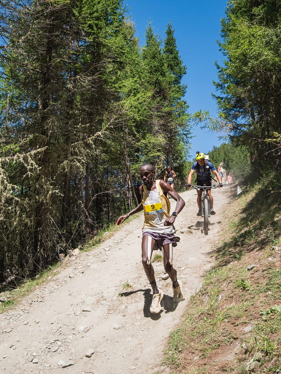 A mountain runner in a race bib running on a gravel path in an Alpine village
