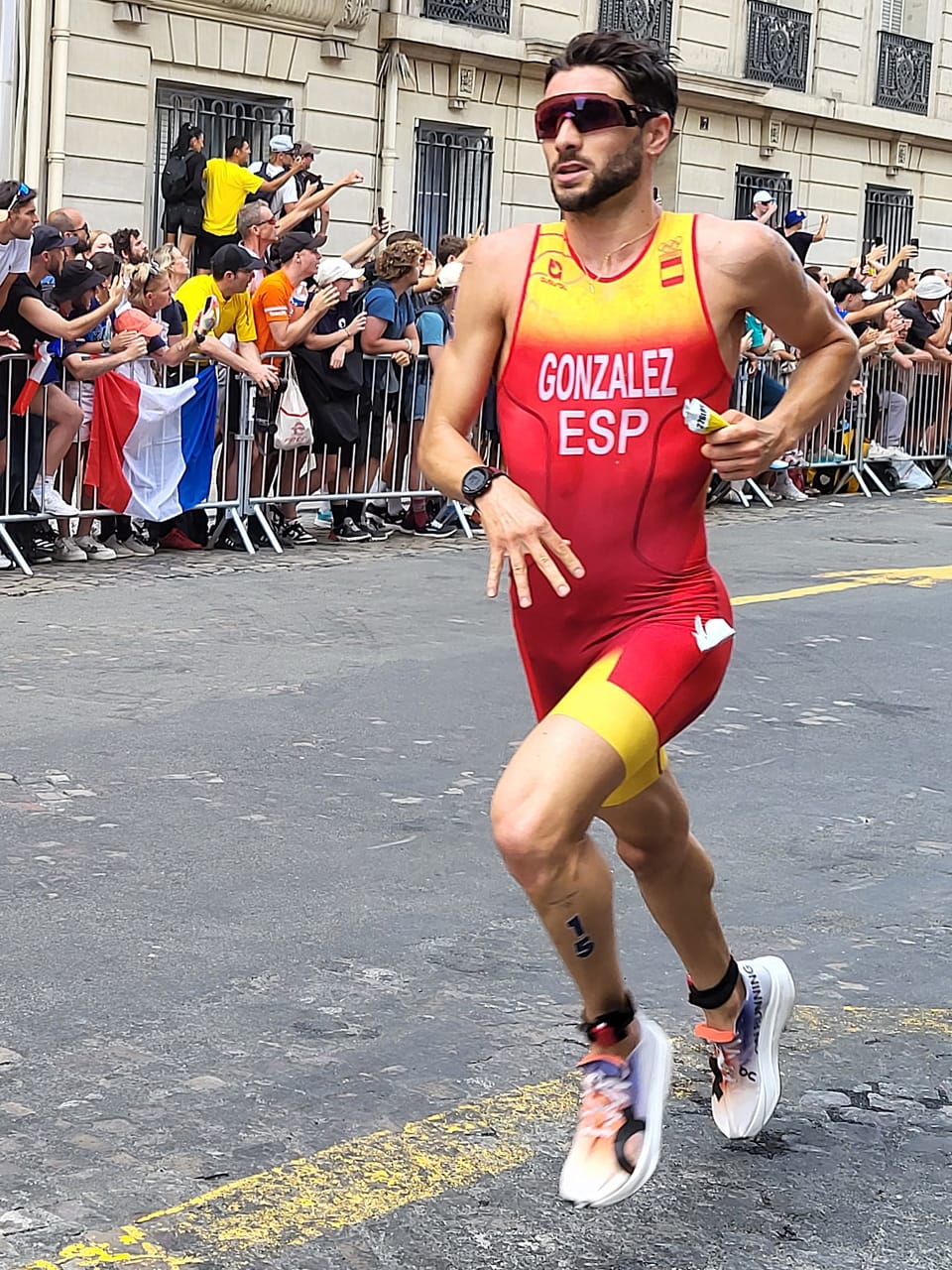 Alberto González in a red and yellow Spain trisuit running past spectators behind barriers